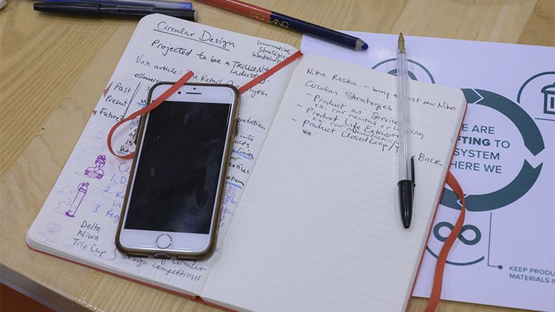 An iPhone, a notebook, and pens spread out on a desk