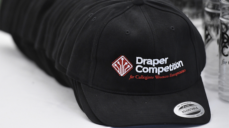 A stack of hats featuring the Draper Competition logo