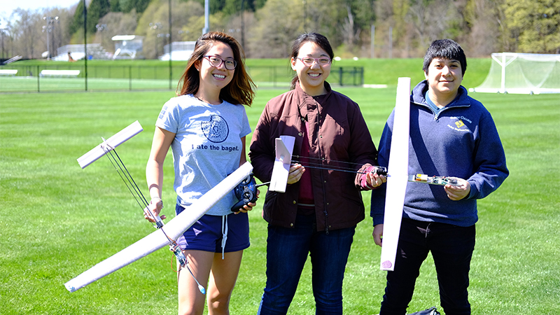 Three students outside holding planes that they built