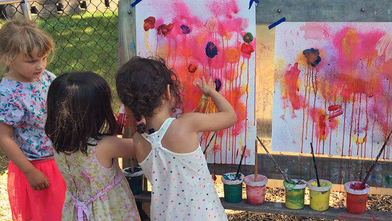 Three girls painting pictures of red flowers