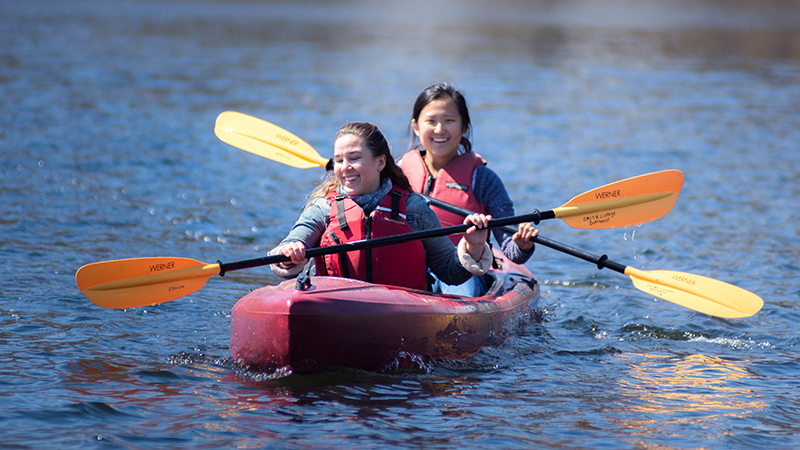 Two students paddling a canoe on the pond