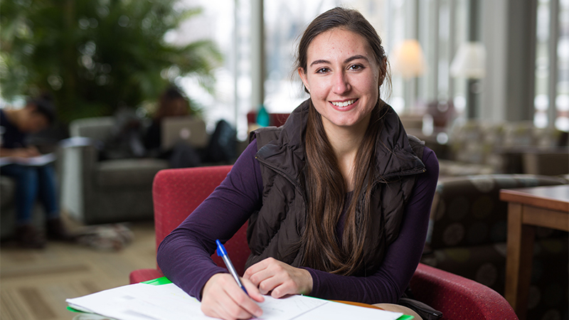 Photo of a smiling student writing in her notebook