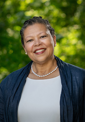 Sarah Willie-LeBreton smiling against a background of green trees.