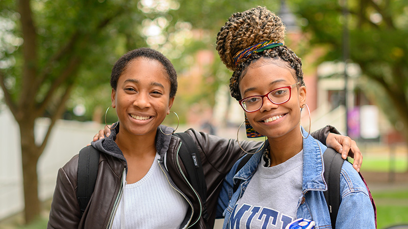 Two students smiling, arms around each other's shoulders