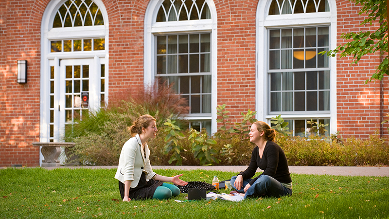 Two students sitting on grass, talking happily