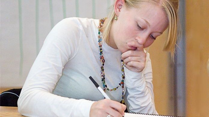 Student in white sweater writing in a notebook