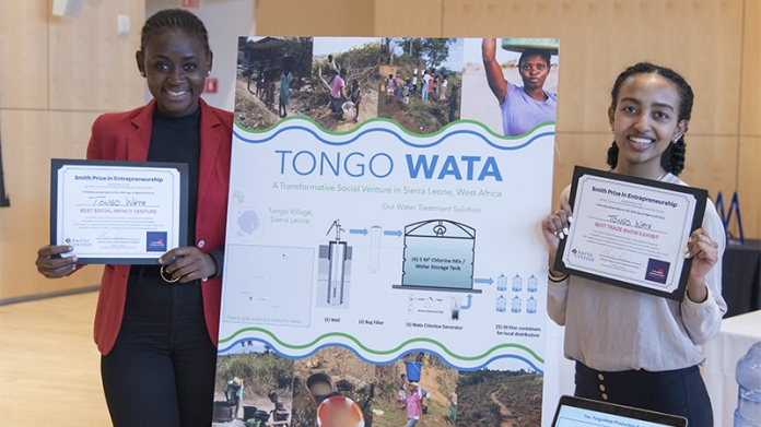 Two students smiling with their project, displaying their winning certificates for the Smith Prize in Entrepreneurship