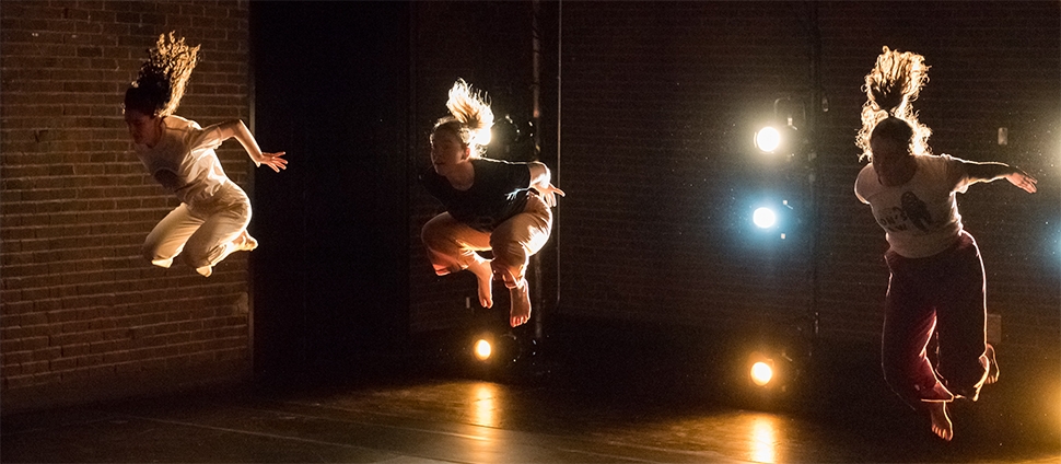 Three dancers mid-air in front of brick backdrops