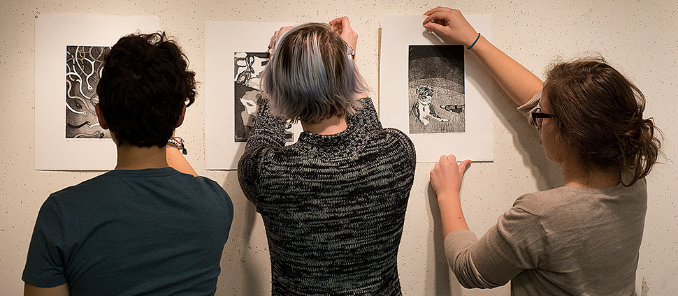 Three students hanging art on a gallery wall