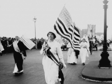 A woman in white carrying an American flag in the 1913 parade on Washington