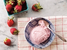 Bowl of strawberry vegan ice cream with fresh strawberries artfully scattered around it.