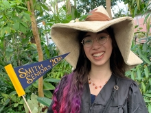 Isabelle Hodge holding "Smithie Seniors 2020" flag in the Lyman Conservatory and wearing a big hat