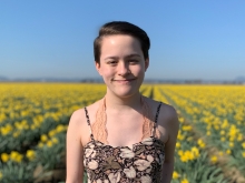 Kristina Chiu smiling in the foreground. In the background is a field of yellow flowers