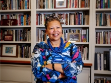 Sarah Willie-LeBreton smiling in front of a bookshelf with her arms crossed