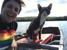 Winter Miller in a rainbow shirt with a gray and white cat on a boat in a lake.