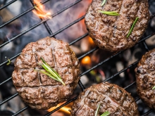 Four hamburger patties cooking on an outdoor grill