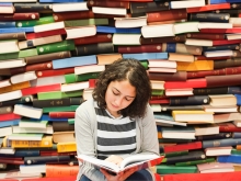 Student reading a book in front of piles of differently colored books