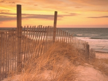 A beach at sunset with a dilapidated fence in the foreground