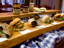 Row of sandwiches and wraps on a wood shelf with condiments on another shelf behind and above