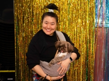 Theater artist Diana Oh holds their dog shovels against a backdrop of shimmering beaded curtains