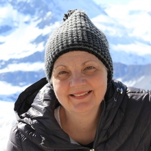 Kathleen Graber smiles in the foreground; in the background a snow-covered mountain looms