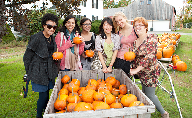 A group of Smith students visiting a pumpkin patch and posing holding pumpkins