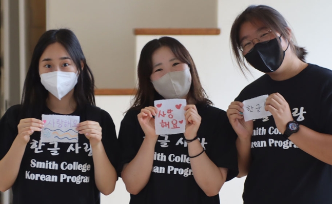 Three students holding up fabric with Korean writing.