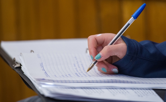 Image of a hand writing in a notebook with a pen