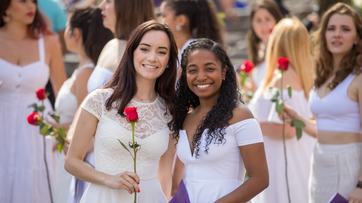 Two students in white Ivy Day dresses holding red roses