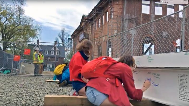 Two students sign the final beam to be installed in the Neilson Library